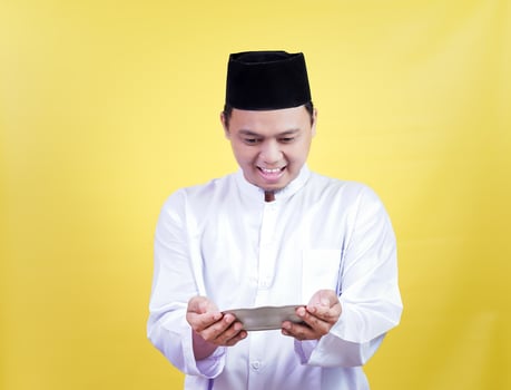 An asian muslim man in traditional attire smiling holds a plate photo
