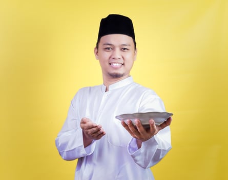 An asian man in traditional attire smiles while holding and presenting a plate photo