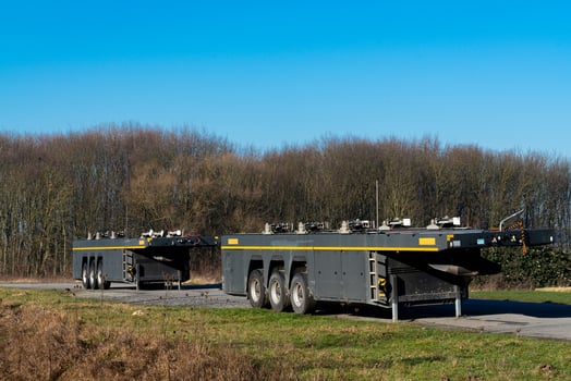 Two heavy machinery trailers parked by a wooded area on a sunny day photo