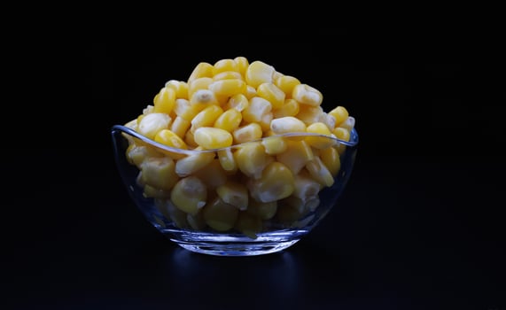 Glass cup full of canned corn kernels on a black background.Canned corn kernels .. photo