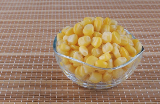 Glass cup with canned corn on a bamboo napkin.Canned corn kernels.. photo