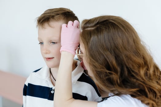 Female doctor examining boy's ear with otoscope in office. Ear cavity treatment health checkup. photo