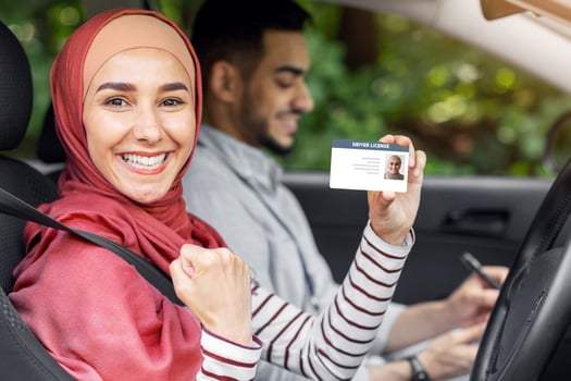 Glad muslim woman in hijab show driving license and fist in open door in car after exam with male teacher, outdoor in summer. Winning gesture, get license, driving test in city, lessons in traffic photo