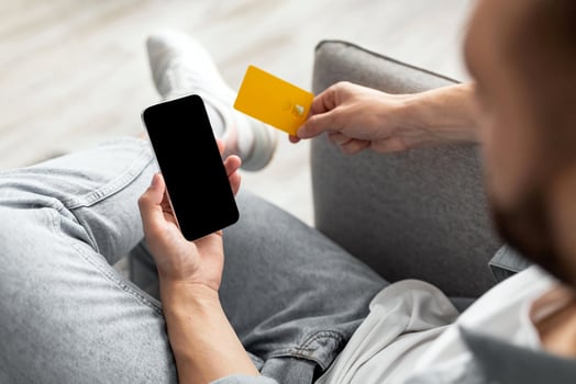 Unrecognizable millennial man with credit card and mobile phone shopping online from home, mockup for app or website. Closeup of young guy buying products in internet photo