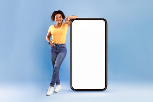 Mobile app advertisement. Happy African American woman leaning on huge smartphone with empty white screen, advertising new website or application, blue studio background photo