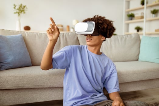 Modern technologies and entertainments. Cool black teen guy in VR headset exploring virtual reality at home, touching imaginary screen, interacting with cyberspace photo