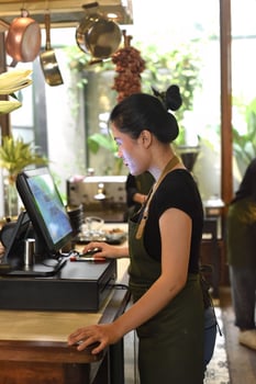 Young Vietnamese waitress working with check out machine in a cafe photo