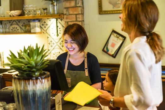 Young Vietnamese waitress works with check out machine and with customers in cafe photo