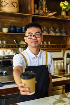 Vietnamese smiling waiter holding paper cup with coffee in a cafe photo