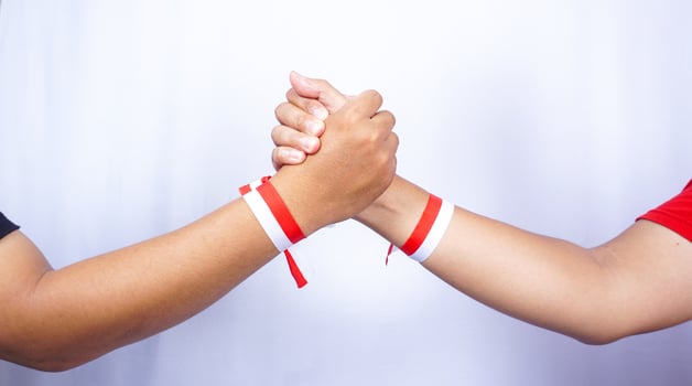 Two Hands with Red and White Ribbons Holding Each Other on White Background photo