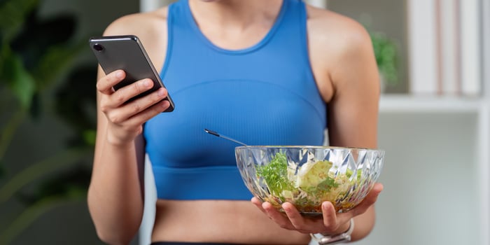 Woman holding a bowl of healthy salad and using her smartphone. photo