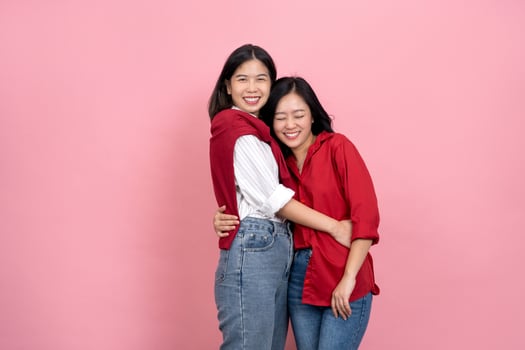 Two Asian girls with long hair in red and white shirts are posing as a LGBTQ couple on a pink background. photo