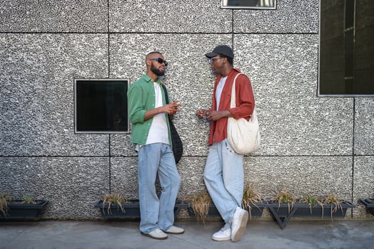 African American student duo engages in lively chat near wall on city walk. Stylish modern youth photo