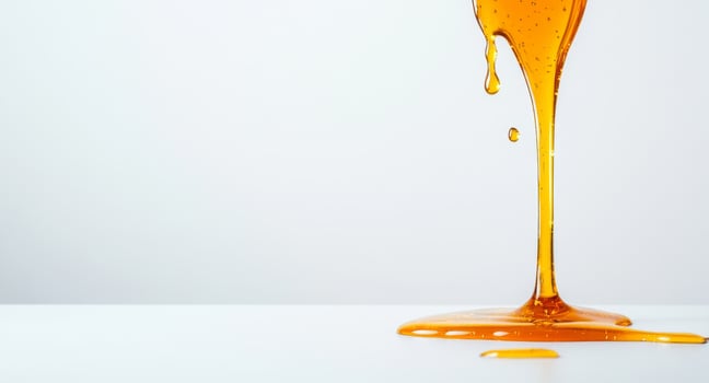 Warm golden honey flows and splashes onto a clean white surface, creating beautiful liquid shapes. The sunlit background enhances the vibrant color, highlighting its smooth texture. photo