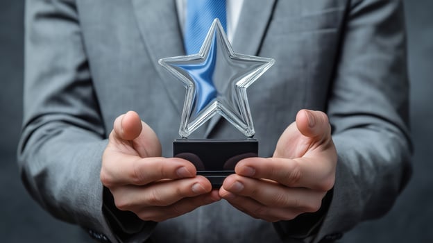 close-up of a man's hands holding a trophy. The man is wearing a grey suit and a blue tie. The trophy is made of clear glass and has a black star-shaped base photo