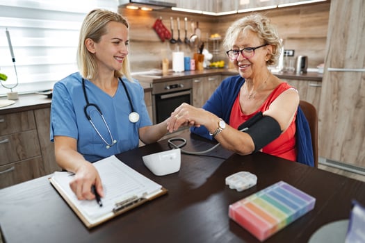 Nurse checks the blood pressure of a cheerful elderly woman in a cozy kitchen photo
