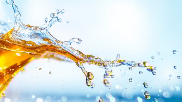 Golden honey splashes into droplets as it collides with a surface, creating vibrant arcs and a striking contrast against a soft blue backdrop. The scene captures the dynamic beauty of flowing liquid. photo