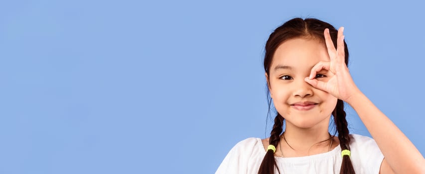 Okay. Asian Little Girl Covering Eye With OK Sign Looking At Camera Posing In Studio On Purple Background. Copy Space photo
