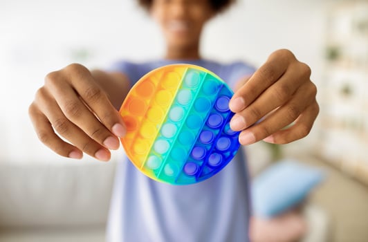 Cropped view of black teenager holding POP IT toy in outstretched hands at home, closeup. Unrecognizable African American youth playing with modern sensory antistress trinket photo