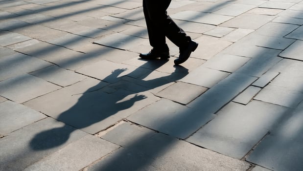 Walking figures cast shadows on cobblestone pavement during late afternoon light photo