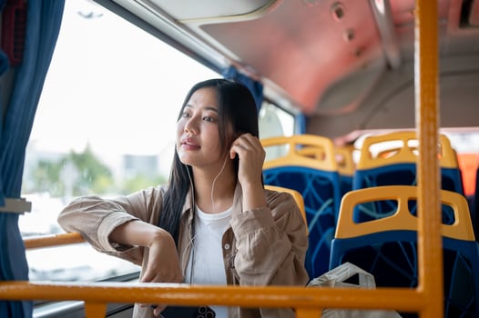 A relaxed Asian woman listens to music while sitting by the window on a bus, commuting in the city. photo