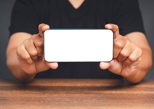 Hands of a man showing a horizontal mobile phone with a blank white screen on a wooden table photo