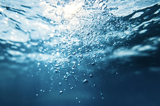 Underwater bubbles rising to surface with sunlight shining through water photo
