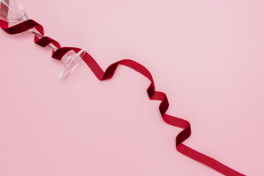 A minimalist and creative composition featuring a wine glass, red velvet ribbon on a soft pink background, representing elegance, Valentines celebration, and sophisticated design. photo