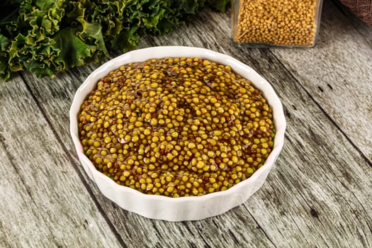 A bowl of mustard on a table next to a bowl of kale photo