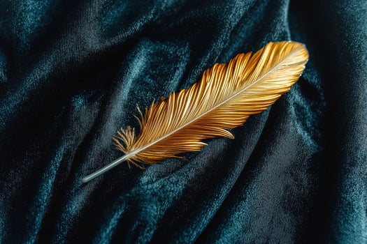 A golden feather resting on dark blue velvet fabric photo