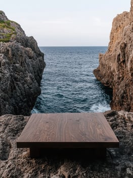 A wooden table sits on a rocky cliff overlooking the ocean photo
