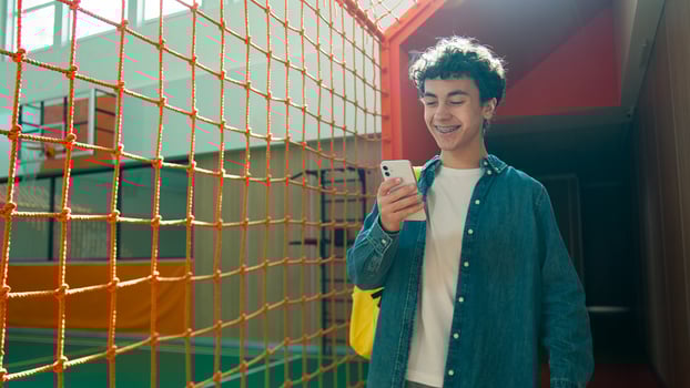 Smiling Caucasian man male happy teenager guy teen student teenage pupil modern technology using mobile phone smartphone app social media online internet in school university walking to sport class photo
