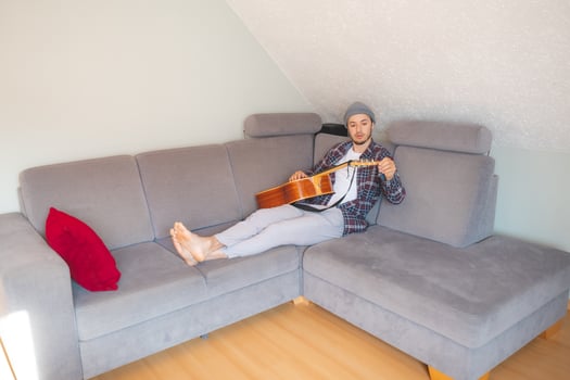 Barefoot musician lies on a gray couch. photo