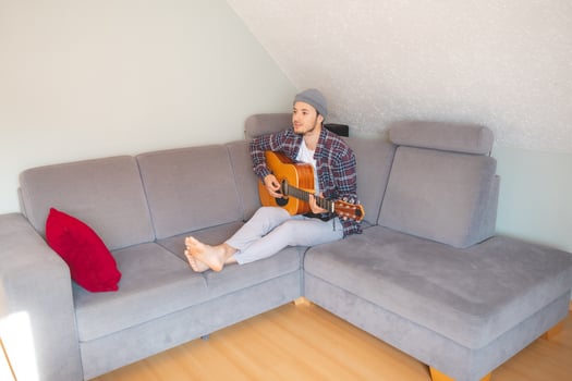 Musician sits comfortably on a gray couch. Guitarist connects with rhythm in peaceful setting photo