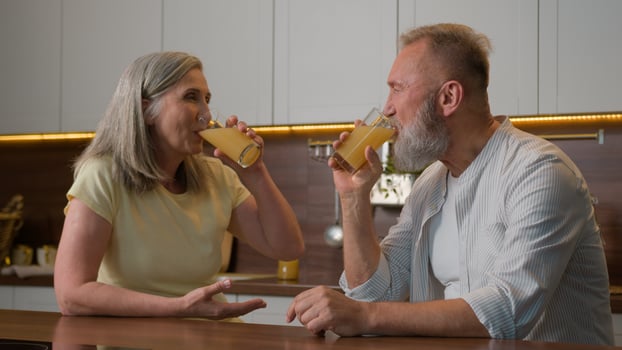 Happy middle-aged old senior couple Caucasian family woman and man drinking orange juice at kitchen home cheerful talk spouses retired wife and husband drink fresh fruit healthy nutrition healthcare photo