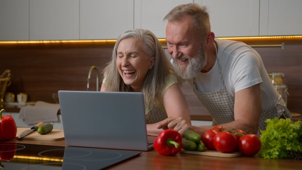 Elder senior old Caucasian couple family with laptop talking at kitchen buy products vegetables online food delivery middle-aged woman and man shopping together watch funny on computer laughing photo