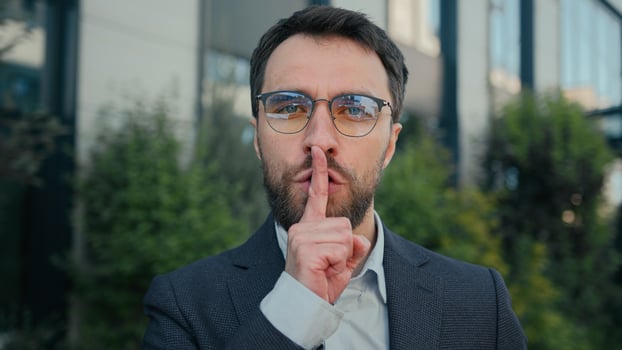 City portrait Caucasian business man businessman outdoors showing silence hush lips gesture keep secret secrecy confidential information stop talk silent quiet put finger to mouth mysterious hand sign photo