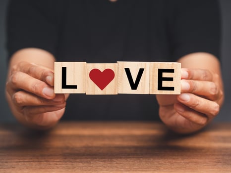 Hands holding wooden cubes with the letters LOVE and red heart icon while sitting at the table photo