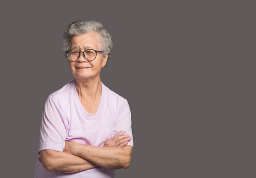 An elderly Asian woman looking at the camera with a smile while standing on a gray background photo