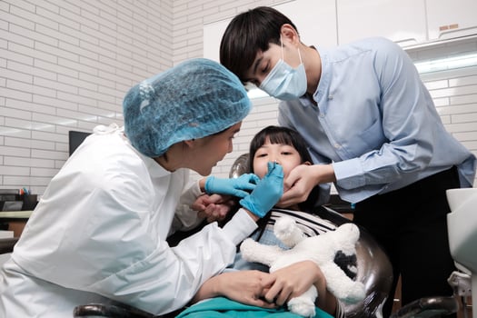 Asian female pediatric dentist examines a girl's teeth in dental clinic with father encourages, mouth oral hygiene, and professional orthodontic healthcare work in a kid hospital. photo