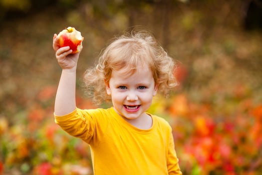 Three year old girl having breakfast in autumn park, drinking tea from a cup with basket of food and fruit nearby. photo