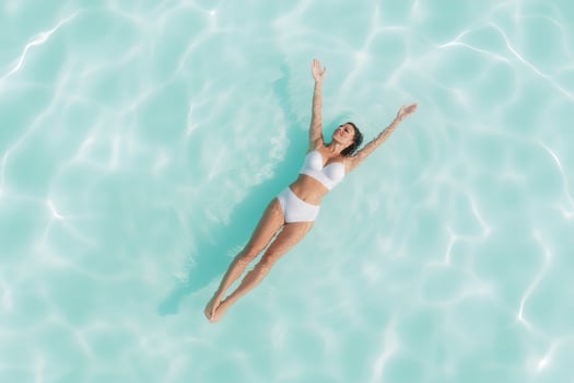 A woman floats effortlessly in clear tropical waters, surrounded by soft ripples. Sun rays filter through, creating a calm, glowing ambiance that enhances the tranquil moment photo