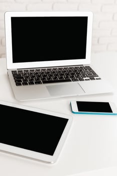 Modern workspace with laptop, tablet, and smartphone on white table in bright room photo