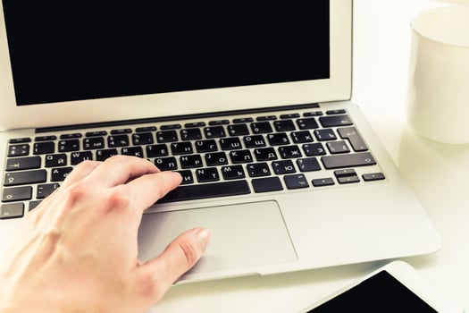 Hand typing on a laptop keyboard while sitting at a desk with a cup nearby in a bright workspace photo