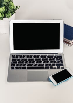 Workspace with a laptop and smartphone placed on a table beside a plant and notebook in a bright setting photo