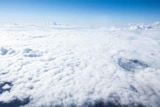 Cloudscape viewed from above during daytime flight shows a vast expanse of fluffy clouds against a clear blue sky photo