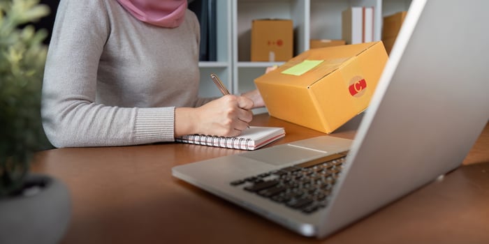 Muslim woman managing online sales while taking notes at her workspace, showcasing e-commerce entrepreneurship. photo