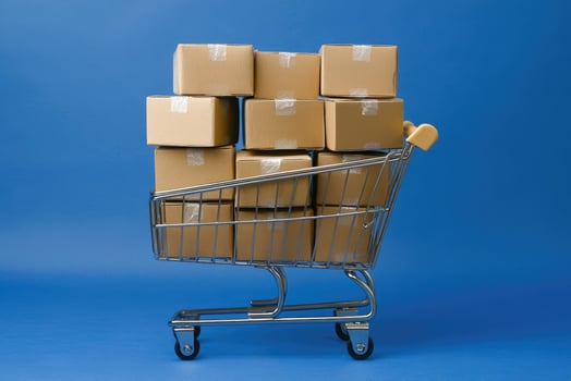 Stacked cardboard boxes in shopping cart against blue photo