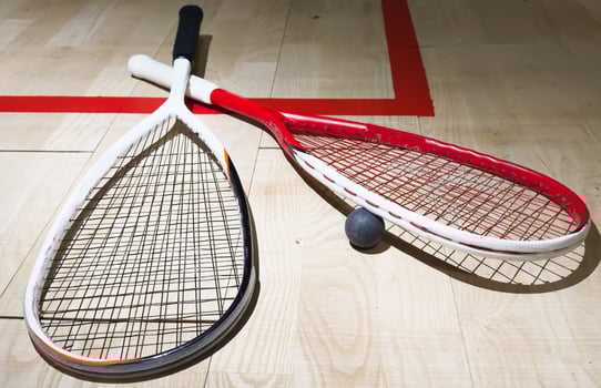 Two rackets and two squash balls lie on the parquet floor. Horizontal photo