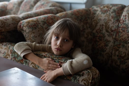 Sad little girl hiding behind sofa at home. Domestic violence concept photo